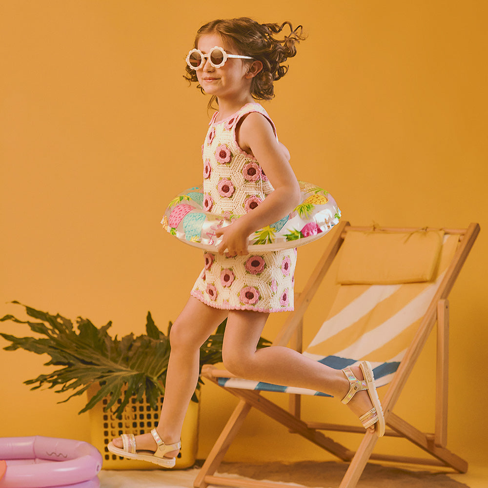 Niña saltando usando sandalias Coqueta y Audaz con efecto tornasol, en ambiente de verano con inflable y look infantil cómodo y colorido. ¡A disfrutar!